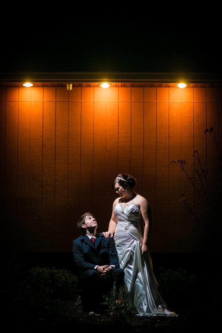 Groom sitting on tree stump and bride standing at night